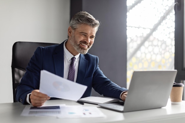 Imprenditore di successo di mezza età che lavora con laptop e documenti in un ufficio moderno