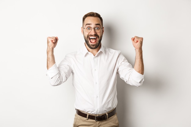 Imprenditore di successo gioendo, alzando le mani e celebrando la vittoria, vincendo qualcosa, in piedi su sfondo bianco.