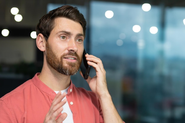 Imprenditore di successo in una camicia rossa che parla al telefono all'interno dell'ufficio un uomo con la barba a