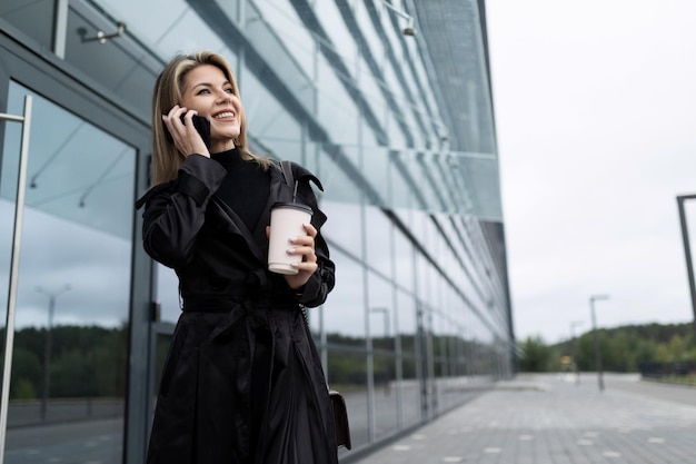 Imprenditore donna con una tazza di caffè sullo sfondo di un edificio in vetro per uffici parlando su a