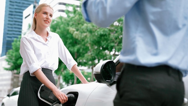 Imprenditore e donna d'affari progressisti installano la spina del caricabatterie dalla stazione di ricarica all'auto elettrica prima di guidare per il centro città Auto ricaricabile ecologica alimentata da energia pulita