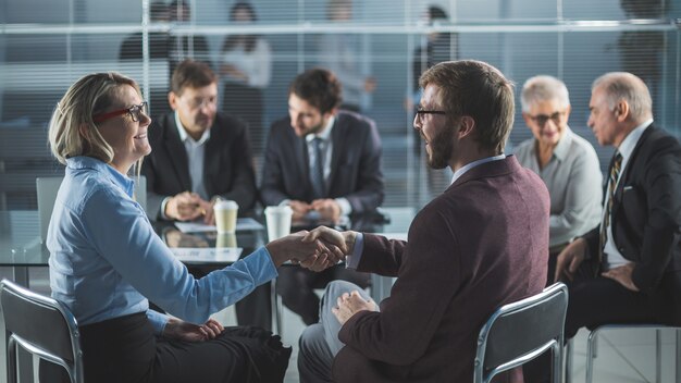 Imprenditore e imprenditrice si stringono la mano seduti al tavolo dell'ufficio. il concetto di cooperazione