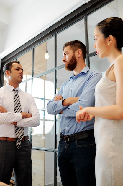 Imprenditore indiano accigliato e fiducioso che parla con i colleghi durante una riunione e chiede del lavoro dei loro dipartimenti