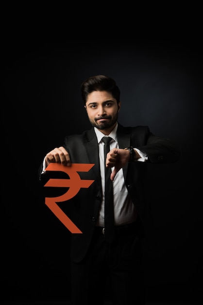 Imprenditore indiano con segno di rupia fatto di carta, in piedi isolato su sfondo nero