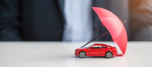 Imprenditore mano che tiene ombrello e copertura auto rossa giocattolo sul tavolo Riparazione di garanzia di assicurazione auto Banche finanziarie e concetto di denaro