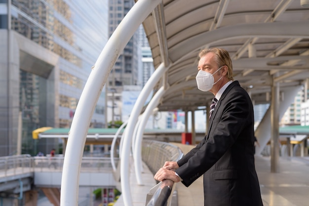 Imprenditore maturo con maschera pensando e guardando la vista della città