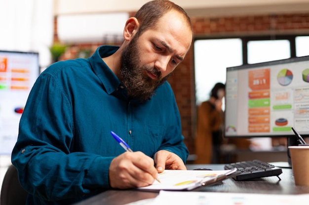 Imprenditore seduto alla scrivania che scrive strategia di marketing analizzando i grafici dei dati utilizzando la presentazione aziendale di pianificazione del computer. Manager alla ricerca di idee per il brainstorming di soluzioni nell'ufficio di avvio