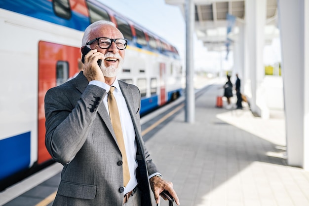 Imprenditore sorridente che parla su smartphone mentre aspetta al binario della stazione ferroviaria