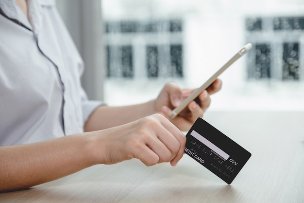 Imprenditore tenere in mano la carta di credito per lo shopping online su smartphone da casa, pagamento e-commerce, internet banking, spendere soldi per le prossime vacanze.