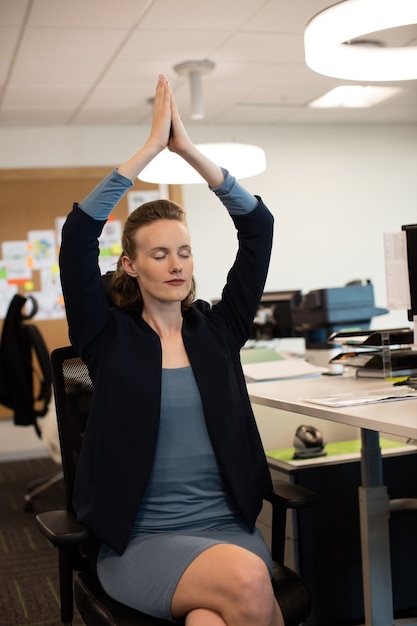 Imprenditrice a praticare yoga mentre è seduto su una sedia