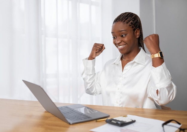 Imprenditrice africana felice ed emozionata seduta sul posto di lavoro che celebra il successo