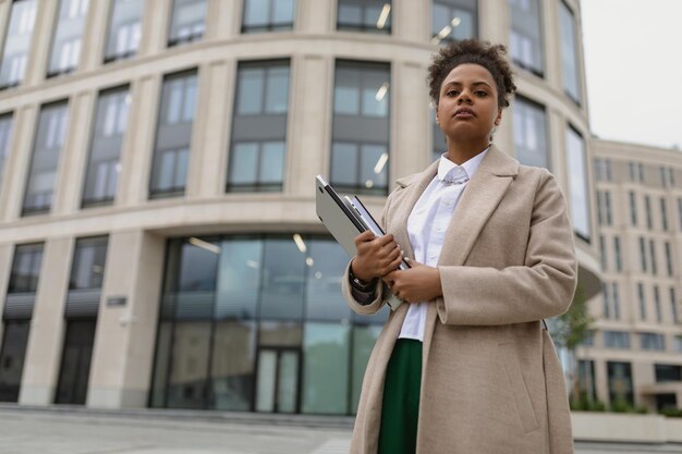 Imprenditrice afroamericana in abiti da lavoro con un laptop in mano contro