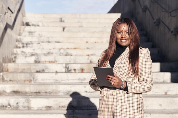 Imprenditrice afroamericana utilizzando una tavoletta Donna sorridente su una scala Copia spazio per il testo