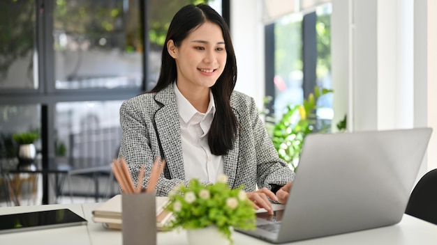 Imprenditrice asiatica di successo digitando sulla tastiera del laptop che lavora nel suo ufficio