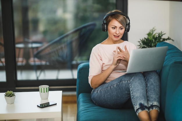 Imprenditrice di mezza età che partecipa a una riunione online sul laptop nel suo ufficio a casa in soggiorno.