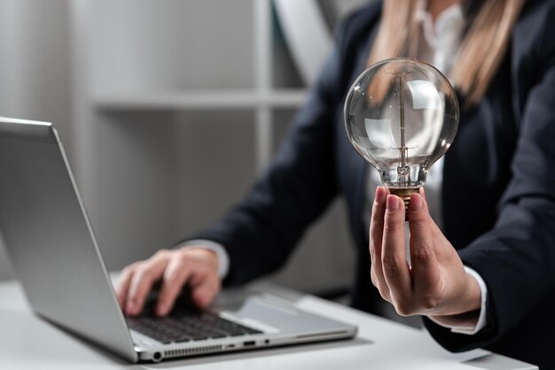 Imprenditrice digitando gli aggiornamenti recenti sul giro in alto sulla scrivania tenendo la lampadina donna in ufficio scrivendo un messaggio importante sul computer Executive inserendo i dati cruciali nel PC