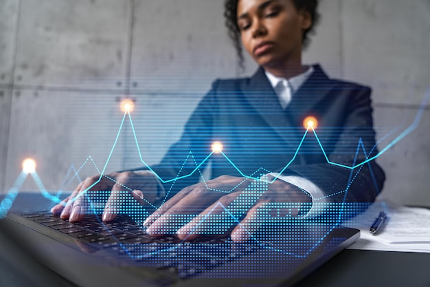 Imprenditrice digitando su laptop lavorare in un ufficio moderno su un nuovo progetto mercato finanziario grafico ologramma doppia esposizione Concetto di successo
