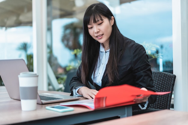 Imprenditrice donna asiatica che lavora e beve caffè all'interno dell'ufficio - Business giovane femmina seduta alla sua scrivania nello spazio di coworking - Tech e concetto di lavoro - Focus sul volto di ragazza