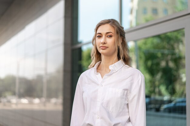 Imprenditrice donna d'affari di successo in piedi all'aperto aziendale esterno dell'edificio. Fiducia caucasica donna d'affari professionale mezza età femminile camicia bianca grande finestra