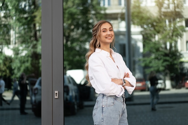 Imprenditrice donna di successo sorridente persona d'affari in piedi all'aperto aziendale esterno dell'edificio felice fiducia caucasica professionale donna d'affari mezza età femmina camicia bianca grande finestra magra