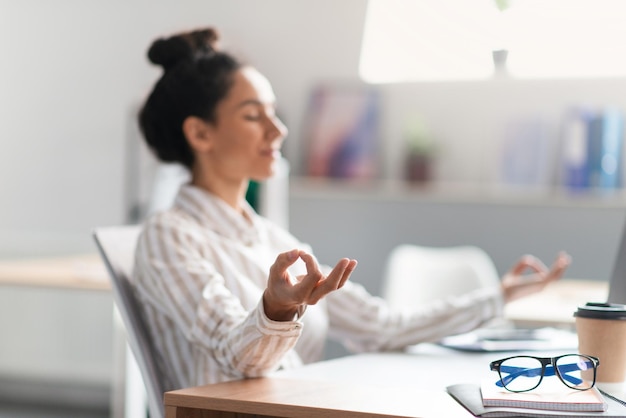 Imprenditrice femminile di gestione dello stress sul posto di lavoro che medita e si rilassa durante una giornata stressante seduta