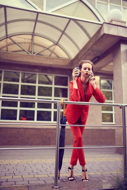 Imprenditrice in costume rosso utilizzando il telefono cellulare vicino a un edificio moderno.