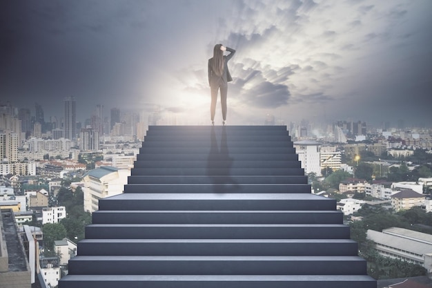 Imprenditrice in piedi in cima alla scalinata di cemento che pensa sopra la città Successo futuro e concetto di crescita