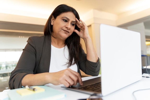 Imprenditrice indiana stanca che utilizza un progetto di lavoro su un computer portatile in ufficio Attività di fallimento