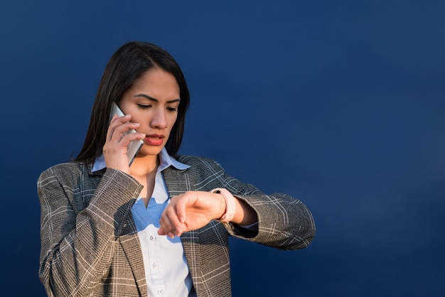 Imprenditrice latina guardando il suo smartwatch e parlando al cellulare su sfondo blu