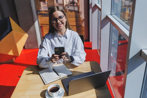 Imprenditrice manager in una camicia bianca che fa lavoro d'ufficio e sorridente capo femminile europeo di successo in occhiali ottici per la correzione della vista in posa a un tavolo in un'area di lavoro