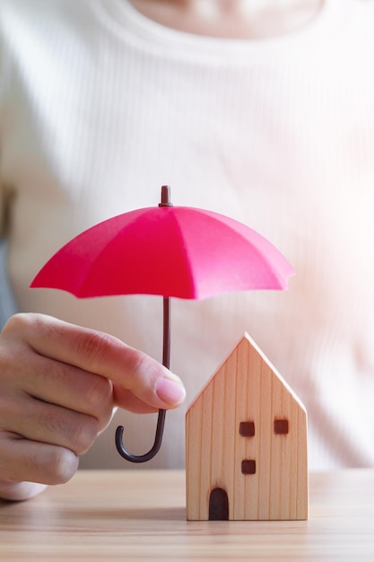 Imprenditrice mano azienda ombrello rosso copertura casa in legno modello di assicurazione immobiliare e concetti di proprietà