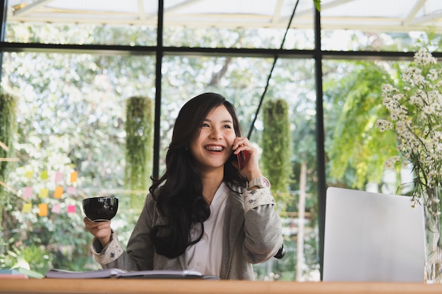 imprenditrice parla sullo smart phone. donna di avvio che tiene tazza di caffè in ufficio.