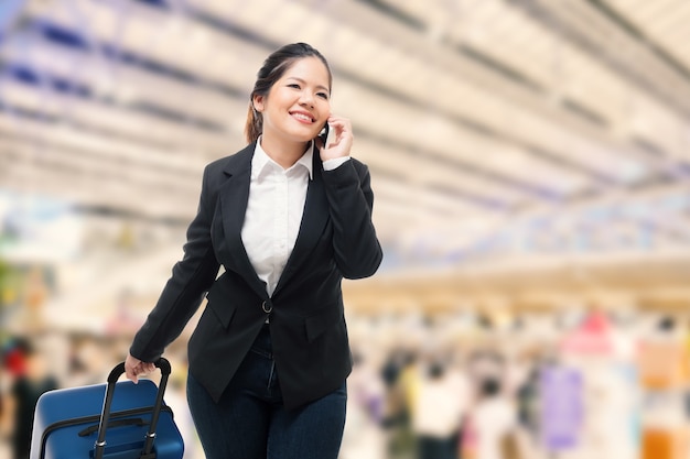 Imprenditrice parlando al telefono cellulare mentre trasporta i bagagli in aeroporto