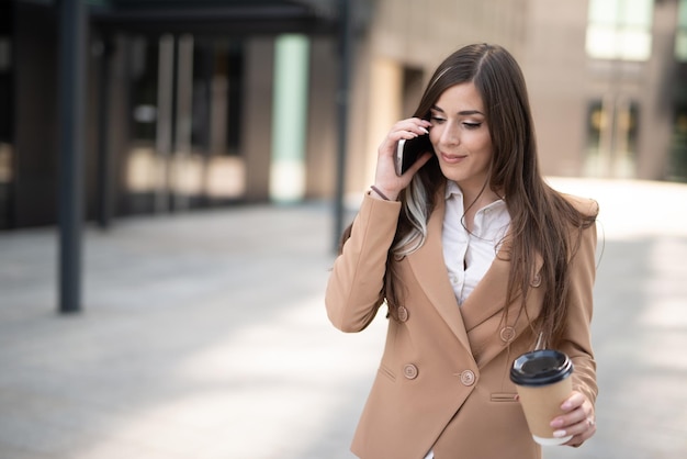 Imprenditrice parlando al telefono in una strada cittadina mentre beve il caffè