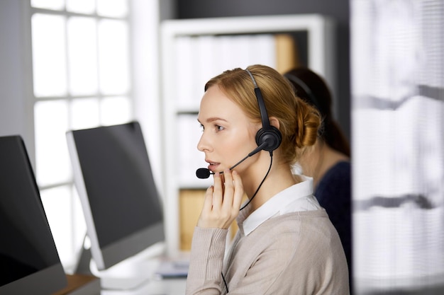 Imprenditrice parlando con l'auricolare mentre è seduto in ufficio. Call center e gruppo di persone diverse nel mondo degli affari.