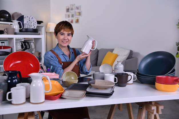 Imprenditrice/proprietaria di una donna asiatica matura che mostra il suo prodotto in ceramica di argilla e lavora a casa