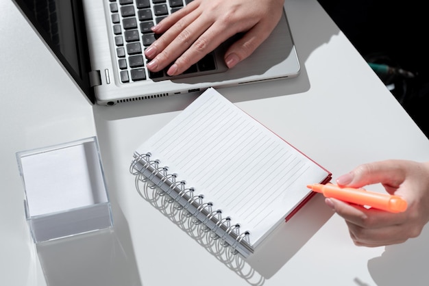 Imprenditrice scrivendo in notebook con pennarello sulla scrivania con note e lap Top donna in tuta con penna colorata sopra il blocco note sul tavolo con appunti e computer