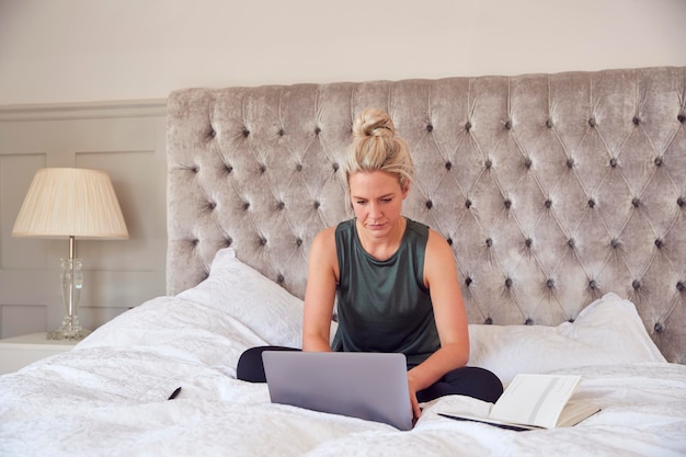 Imprenditrice seduta sul letto con il laptop che lavora da casa in videochiamata durante il blocco pandemico