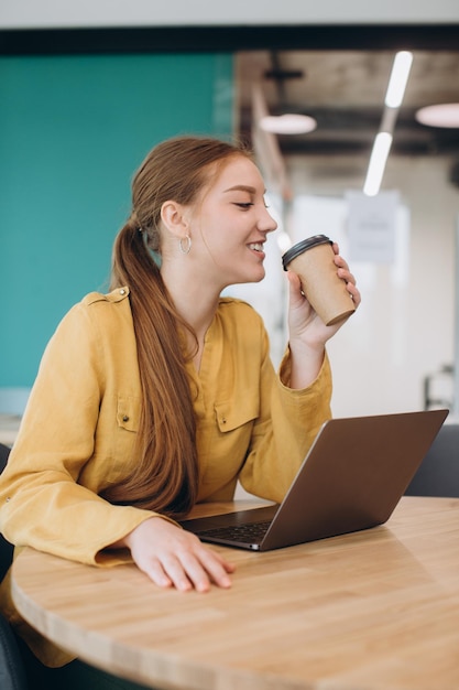 Imprenditrice sorridente con una tazza di caffè seduto alla scrivania in ufficio