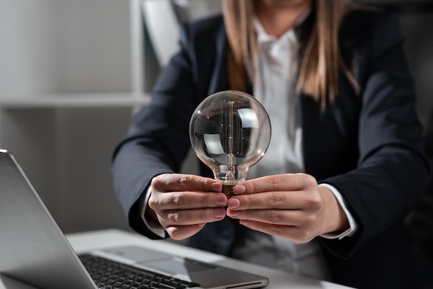 Imprenditrice tenendo la lampadina con entrambe le mani in ufficio donna in tuta avente luce tra i palmi delle mani sulla scrivania con lap top e presentando messaggi importanti