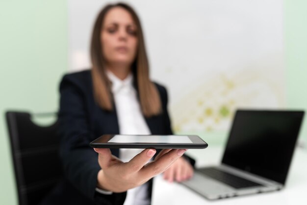 Imprenditrice tenendo tablet con una mano e avendo lap top sulla scrivania donna che presenta importante