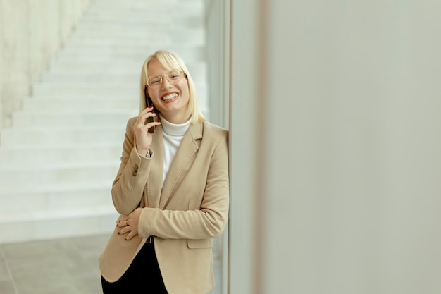 Imprenditrice utilizzando il telefono cellulare sul corridoio dell'ufficio moderno