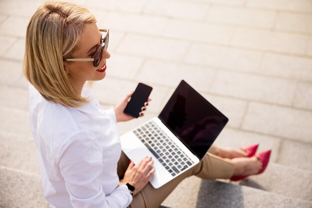 Imprenditrice utilizzando laptop e telefono cellulare mentre è seduto fuori