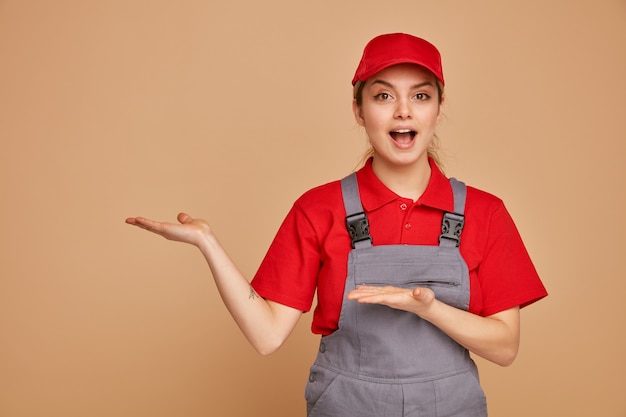 Impressionato giovane operaio edile femminile che indossa cappello e uniforme che punta a lato con le mani