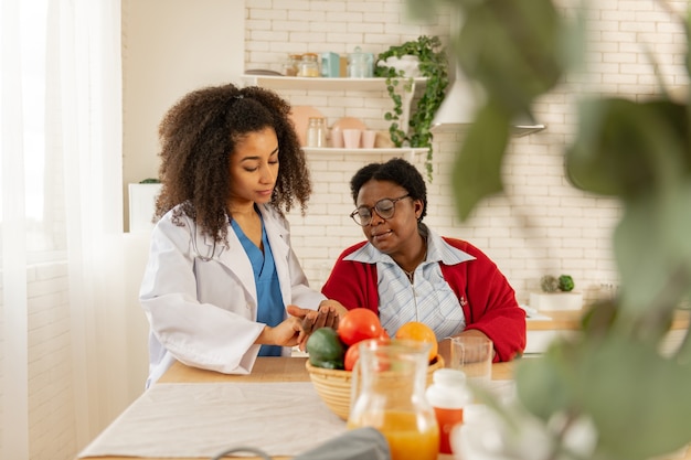 Impulso per il paziente. Assistente medico privato che viene in cucina e misura il polso per il paziente che si sente male