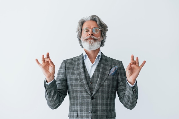 In abiti eleganti In piedi contro il muro bianco Uomo moderno ed elegante con capelli grigi e barba all'interno