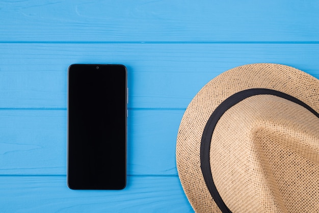 In alto sopra la foto ravvicinata di un cappello femminile di paglia e un telefono nero con touchscreen vuoto isolato su uno sfondo di legno di colore brillante