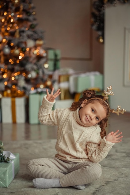 In attesa del nuovo ritratto emozionale di una bambina a casa in una stanza vicino all'albero di Natale con un regalo tra le mani