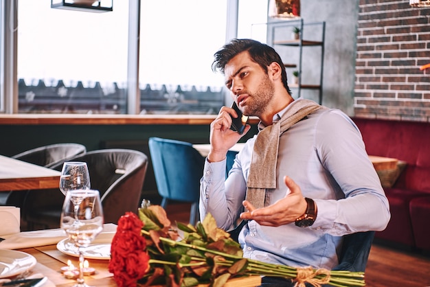 In attesa di fidanzata. L'uomo sta parlando tramite smartphone mentre aspetta al ristorante la sua ragazza. Le rose rosse sono sdraiate sul tavolo.