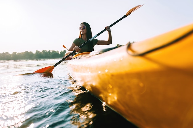 In cerca di avventure. Vista ad angolo basso di bella giovane donna sorridente che fa kayak sul lago e sorride